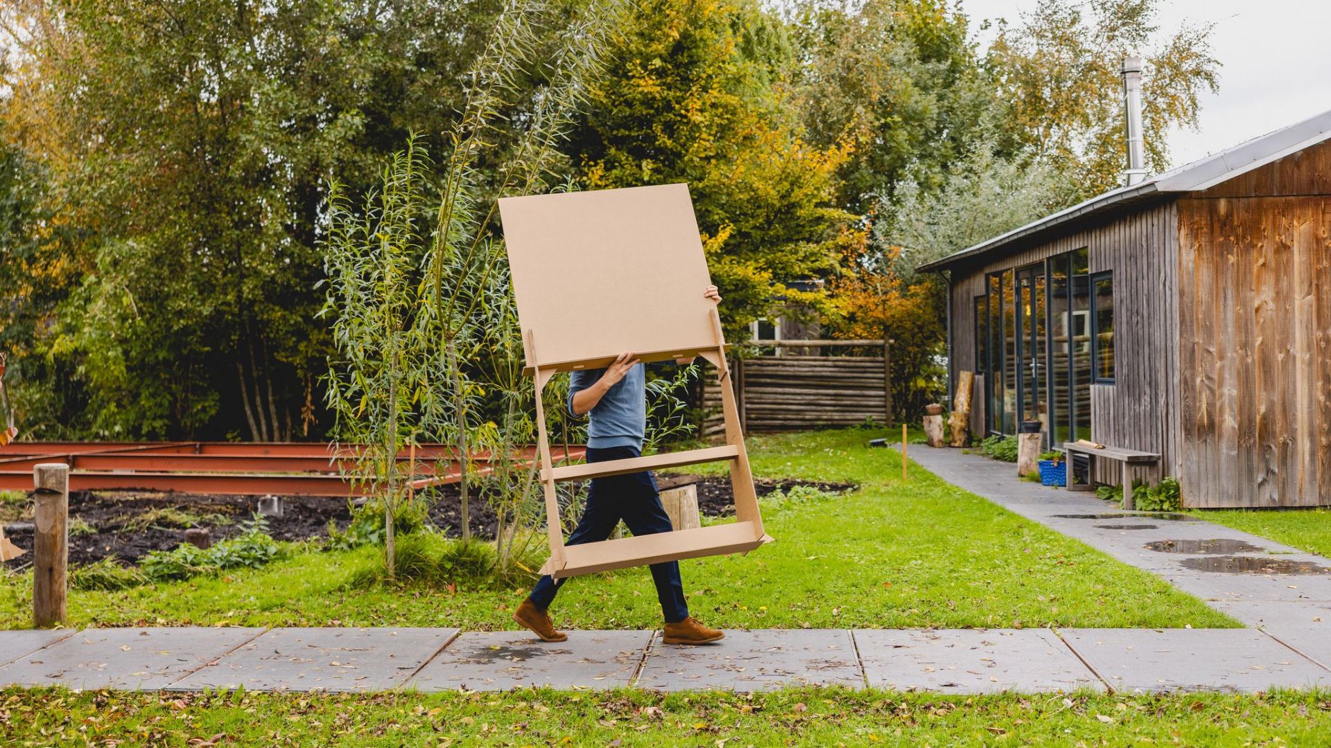 Man die een groot kartonnen bord door de tuin draagt in de herfst