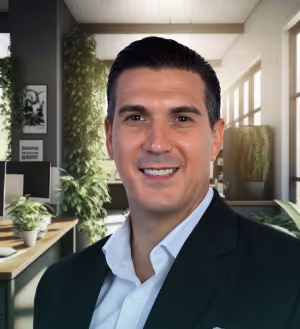 Smiling man with dark hair wearing a white shirt and dark blazer in a bright office with plants.