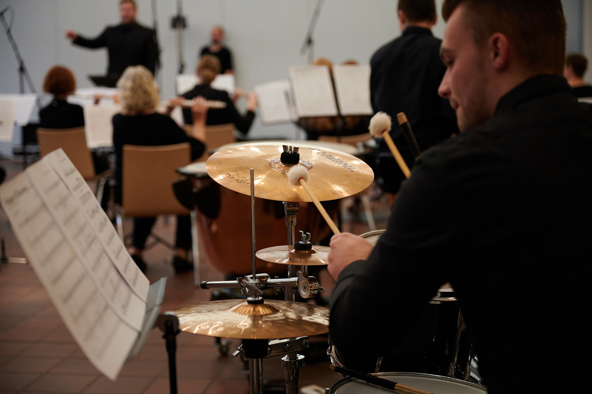 Schlagzeuger des Perflu Orchesters spielt während eines Konzerts, im Hintergrund sind Dirigent und Holzbläser zu sehen