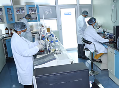 Three lab technicians in white coats and hairnets working in a laboratory with various glassware and equipment.