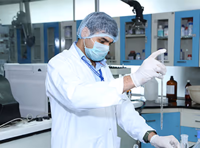 Male scientist in a lab coat, hair net, face mask, and gloves working with a pipette in a laboratory.