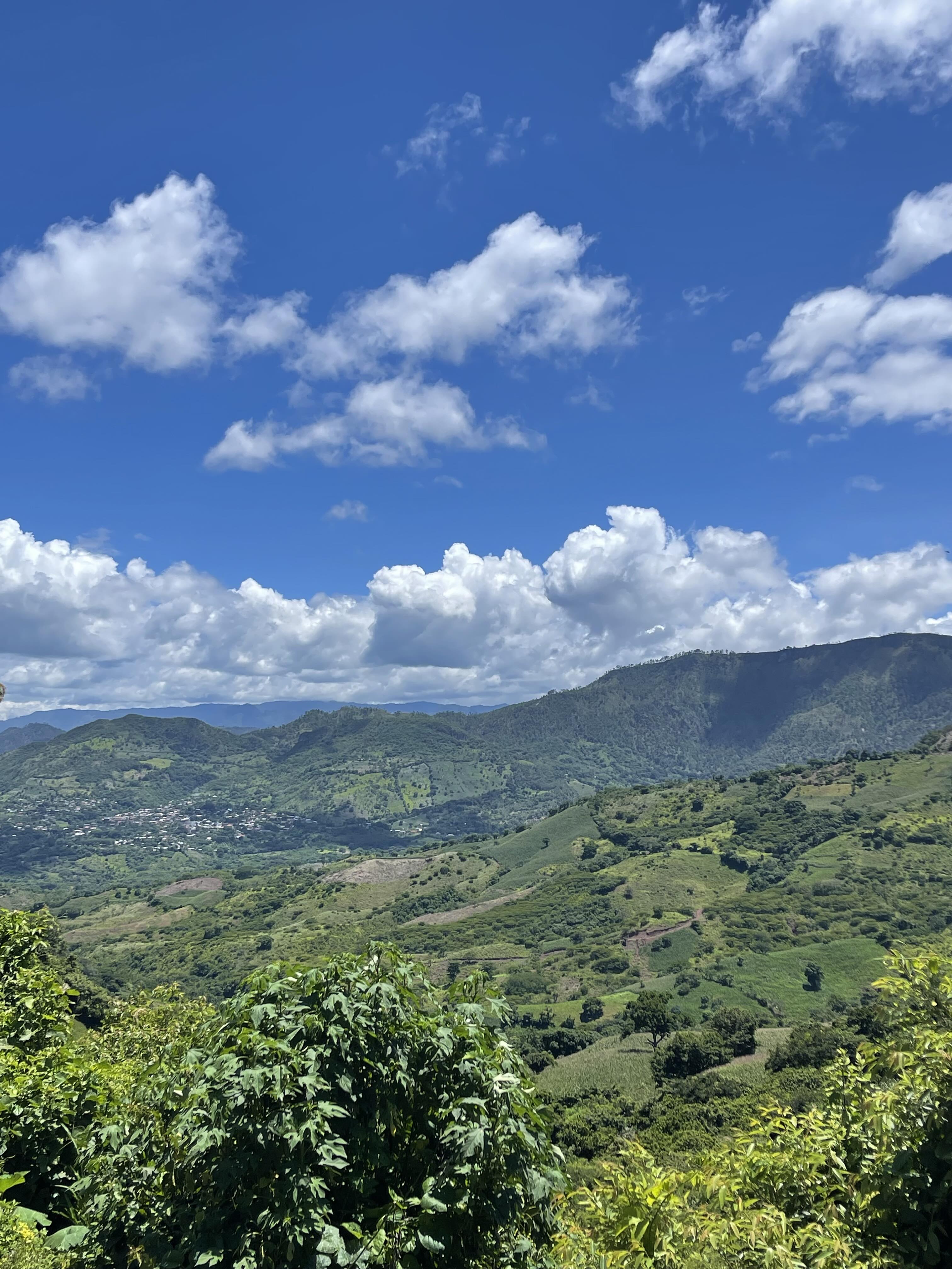 Lush green hills and mountains under a bright blue sky with scattered white clouds.