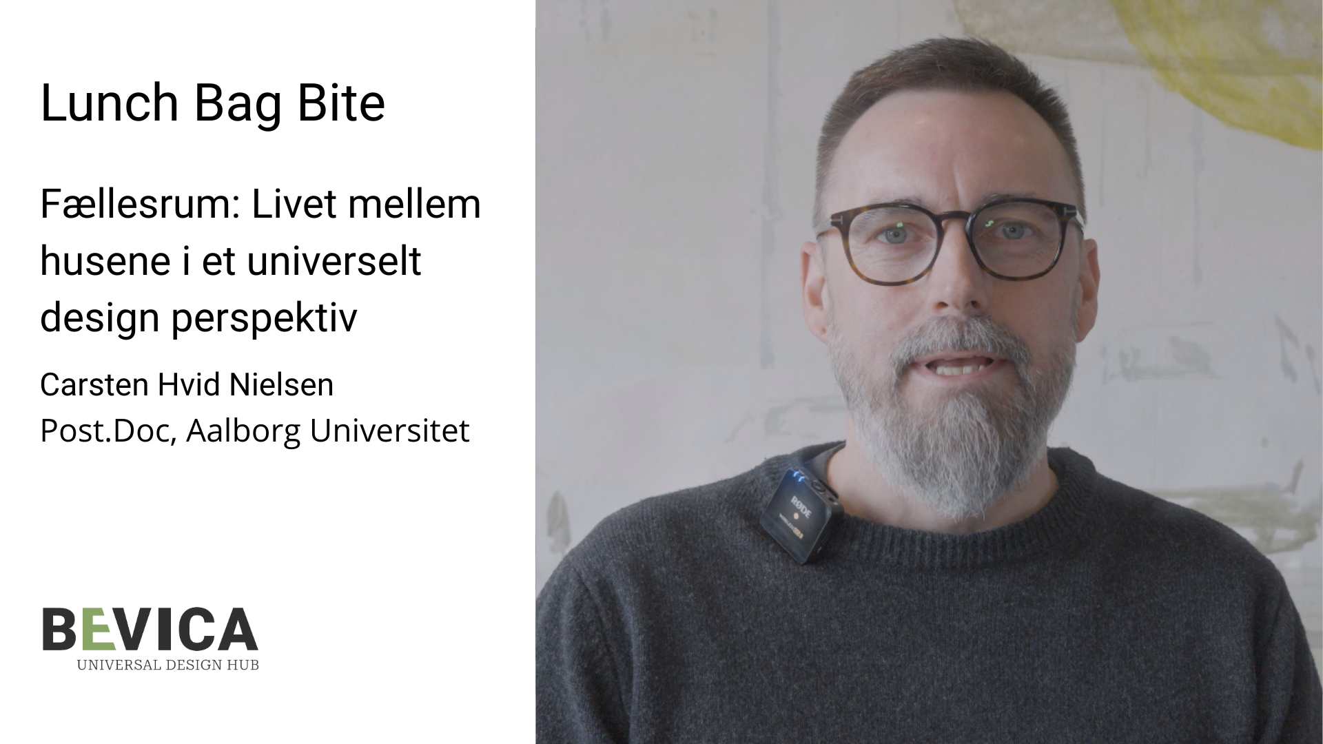 Stillbillede fra en videooptagelse af en mand med kort gråt hår, skæg og runde briller, iført en mørk striktrøje