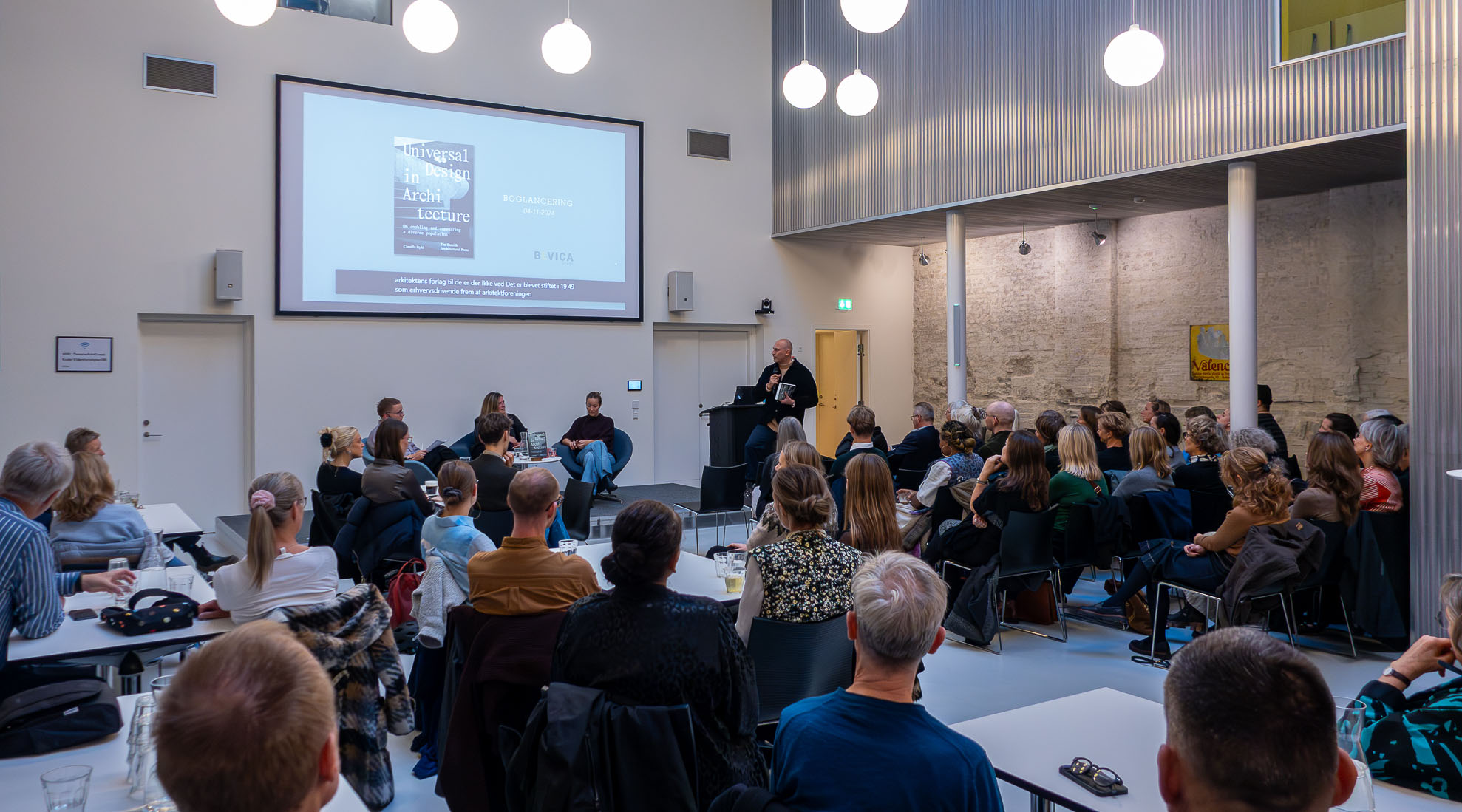 En samling mennesker deltager til et møde i en stor lys sal