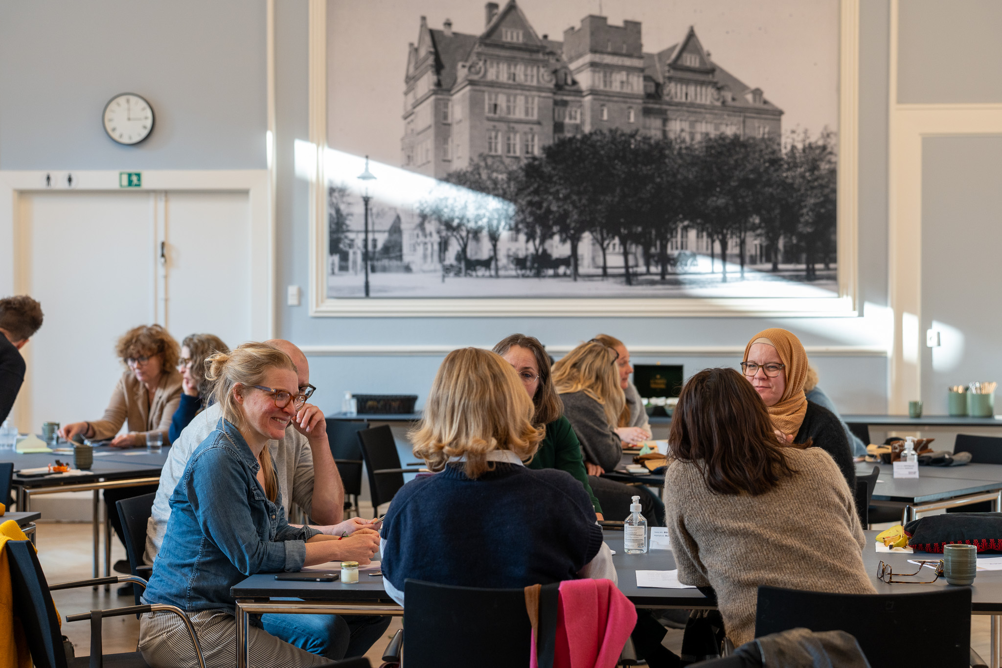 Medarbejdere fra Landsbyggefonden deltager i workshop om universelt design og sidder i grupper omkring borde i et mødelokale.