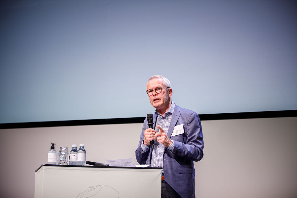 Thomas Sinkjær is standing on a stage speaking into a microphone.