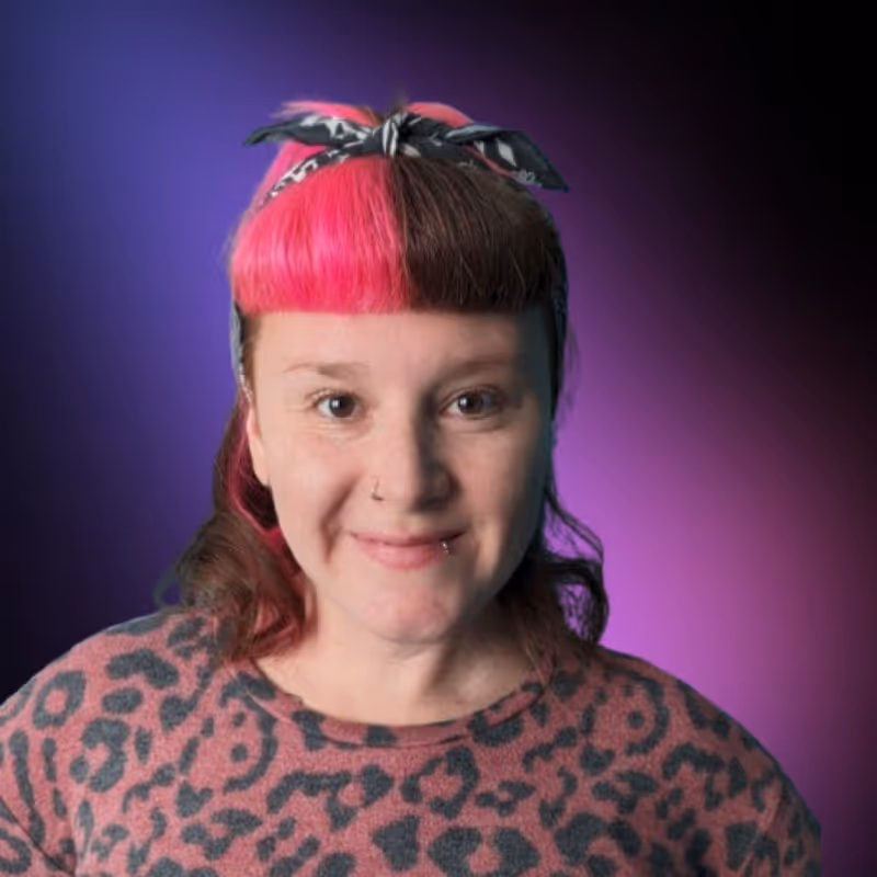 Smiling woman with half bright pink and half brown hair, wearing a leopard print top and a patterned headband against a purple gradient background.