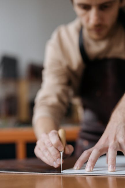 Close-up of a craftsman precisely marking wood with a chisel indoors, showcasing skilled hands and tools.
