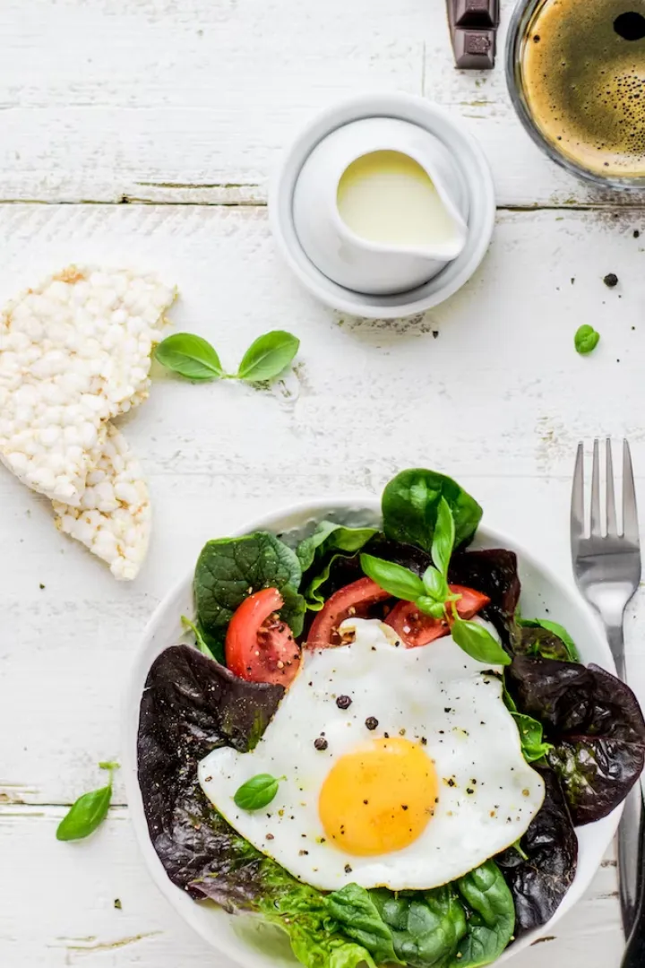 Protein-rich breakfast with fried egg, leafy greens, and tomatoes on a white plate