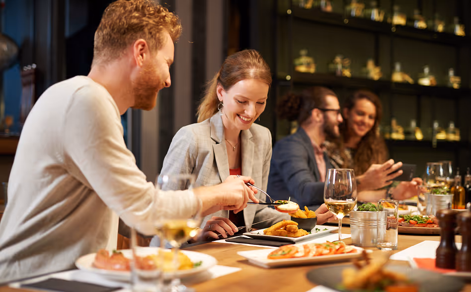 A group of four people enjoying a meal together at a restaurant table with various dishes and wine glasses.