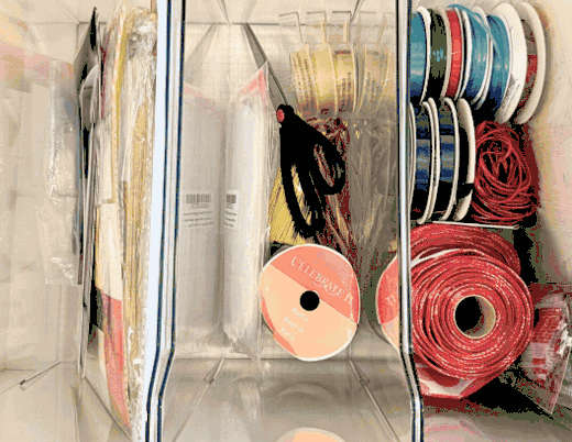 Animated demo of an organized gift wrap station with vertical paper roll storage and labeled bins for ribbon, tags, and tape