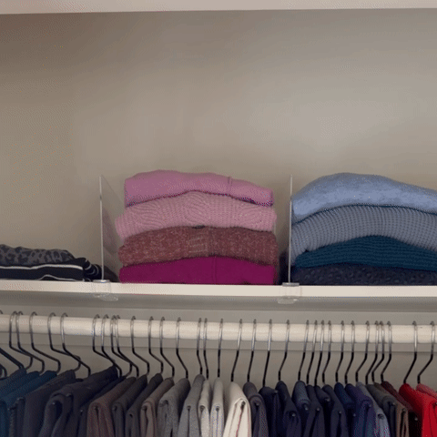 Folded sweaters separated by clear acrylic shelf dividers on a closet shelf