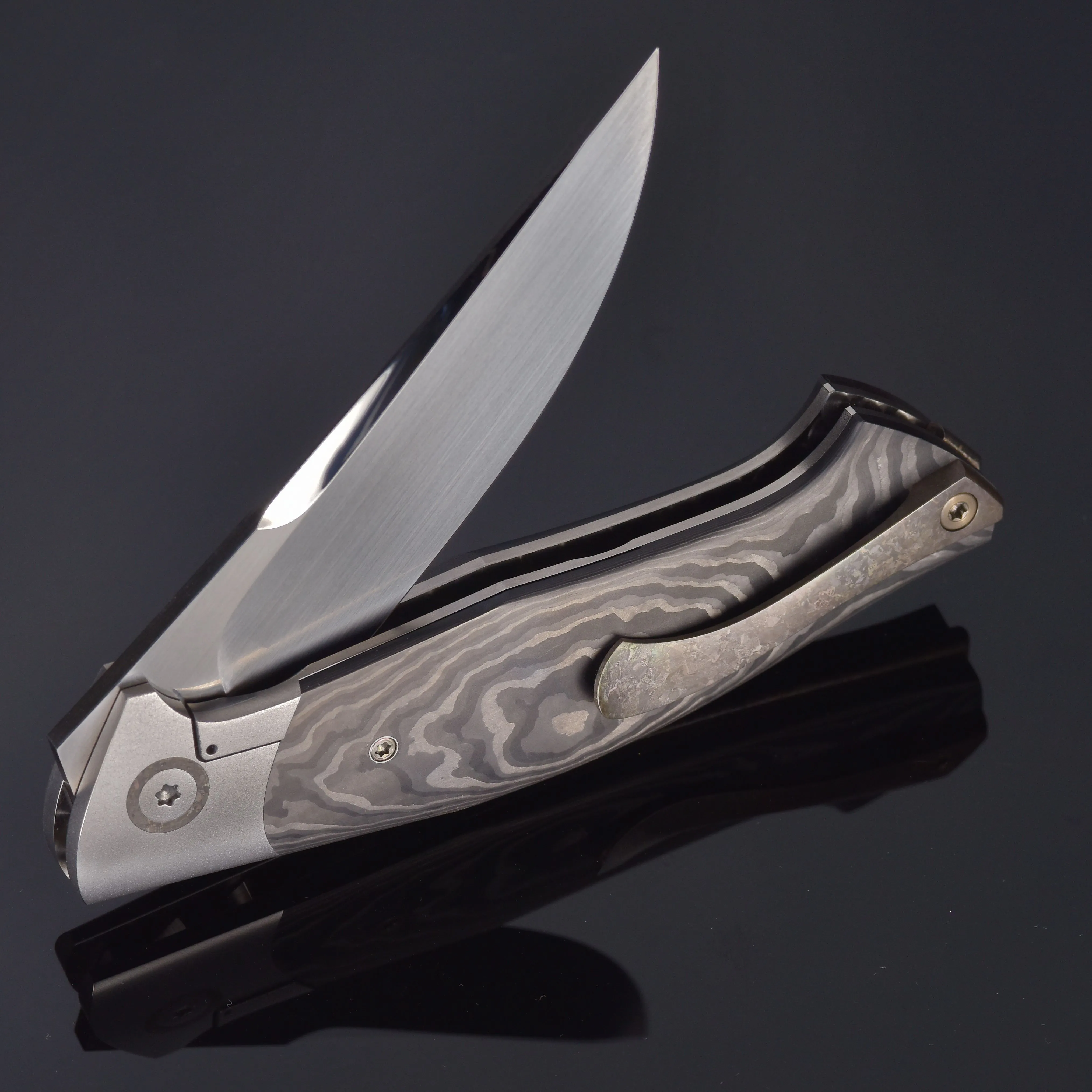 Couteau pliant à lame brillante et manche à motif en acier damassé sur fond sombre.
