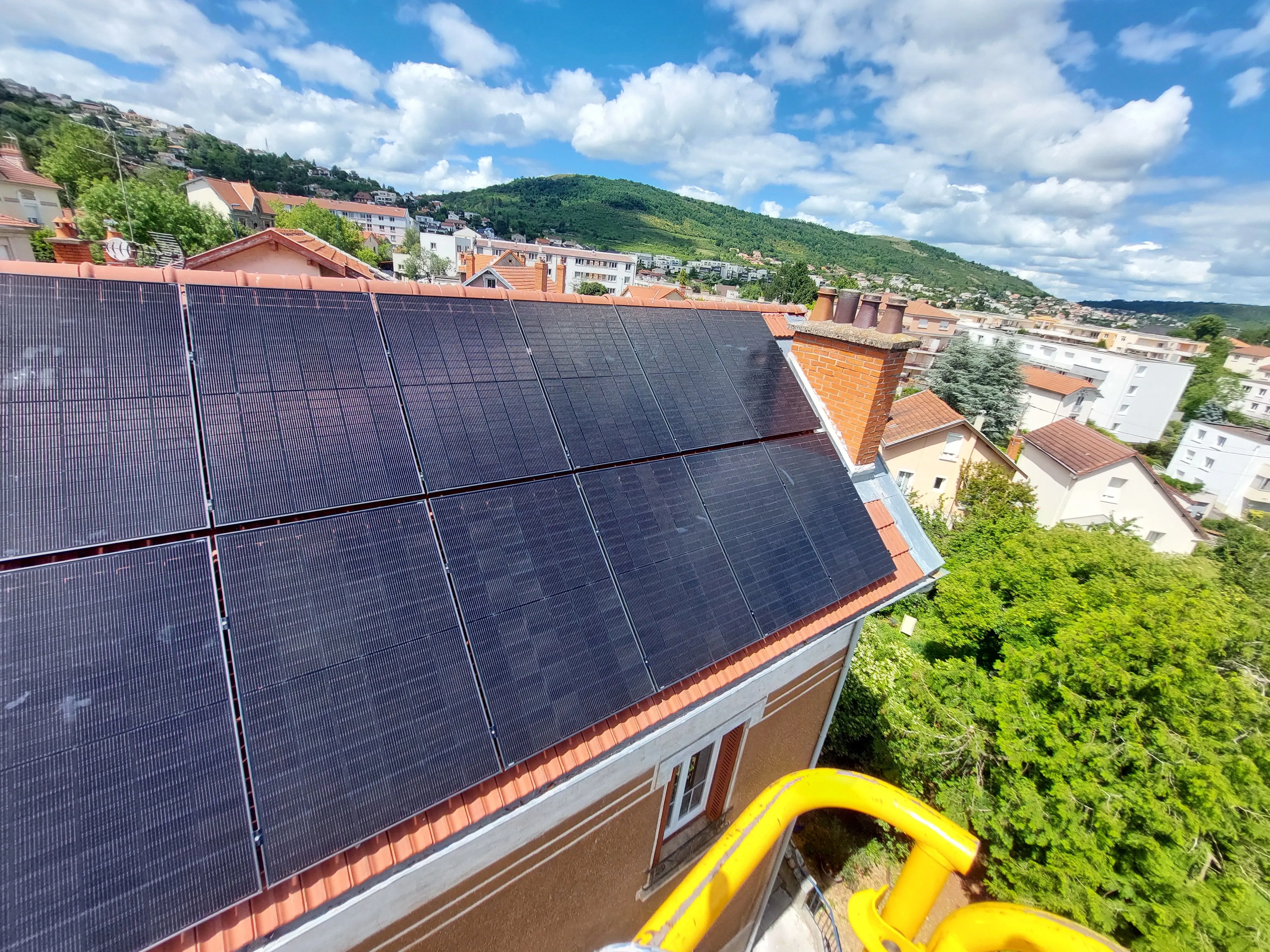 Panneaux solaires installés sur le toit d'une maison avec vue sur des collines et un ciel nuageux.
