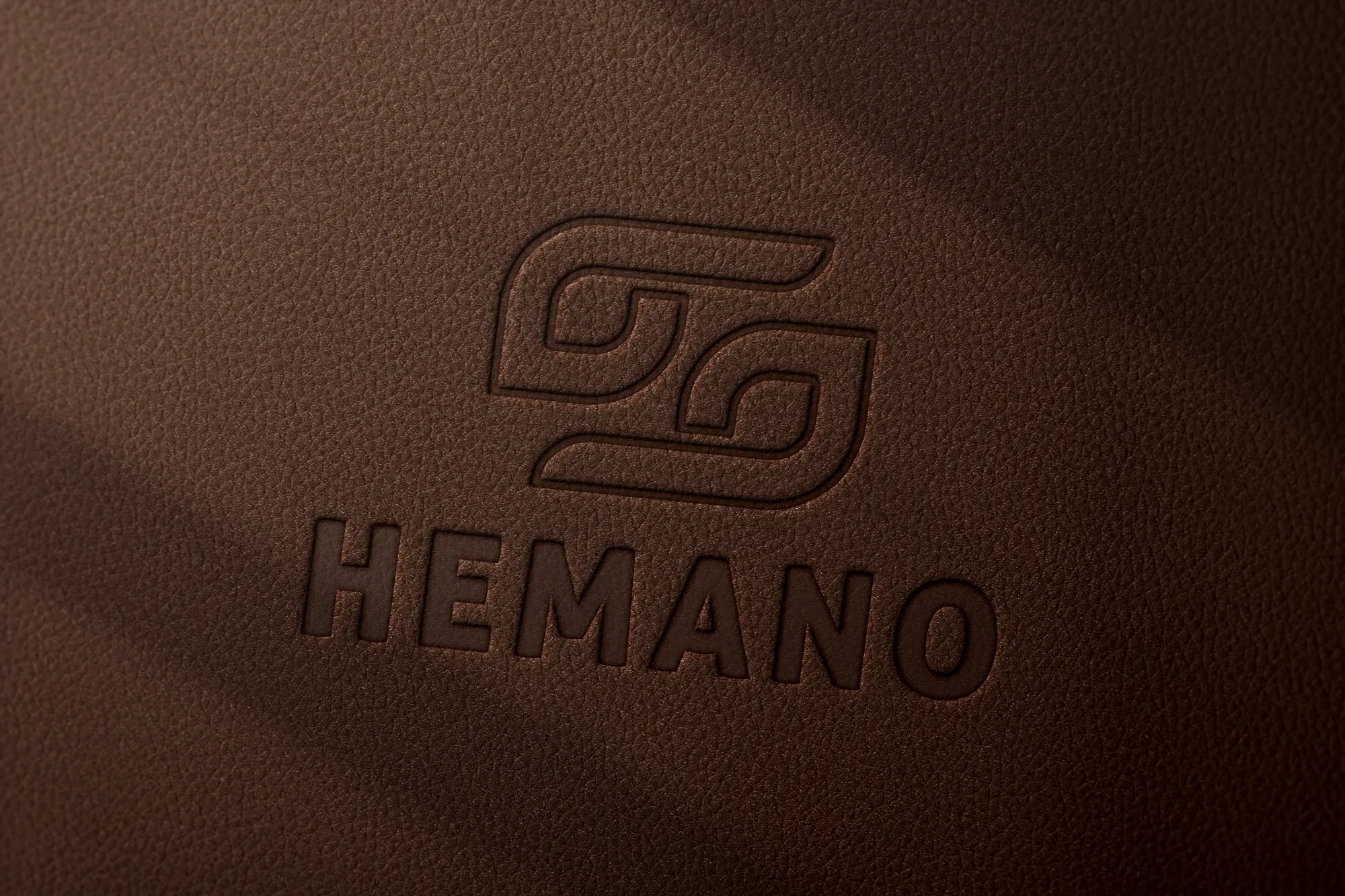 Embossed HEMANO logo on textured brown leather surface.