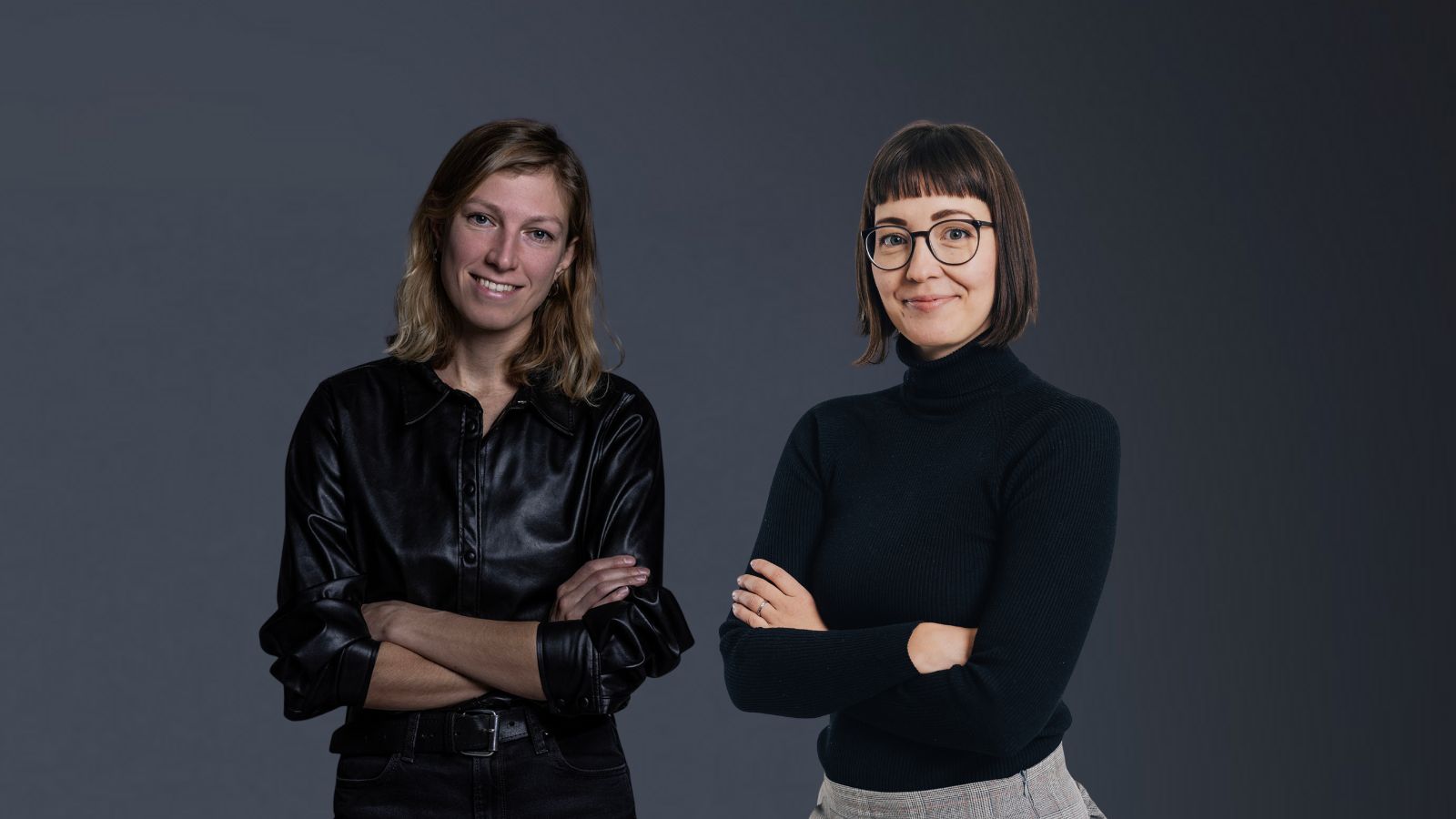 Uudet tuottajat, Anita Parri ja Asta Elijoki seisovat kädet puuskassa harmaalla taustalla.