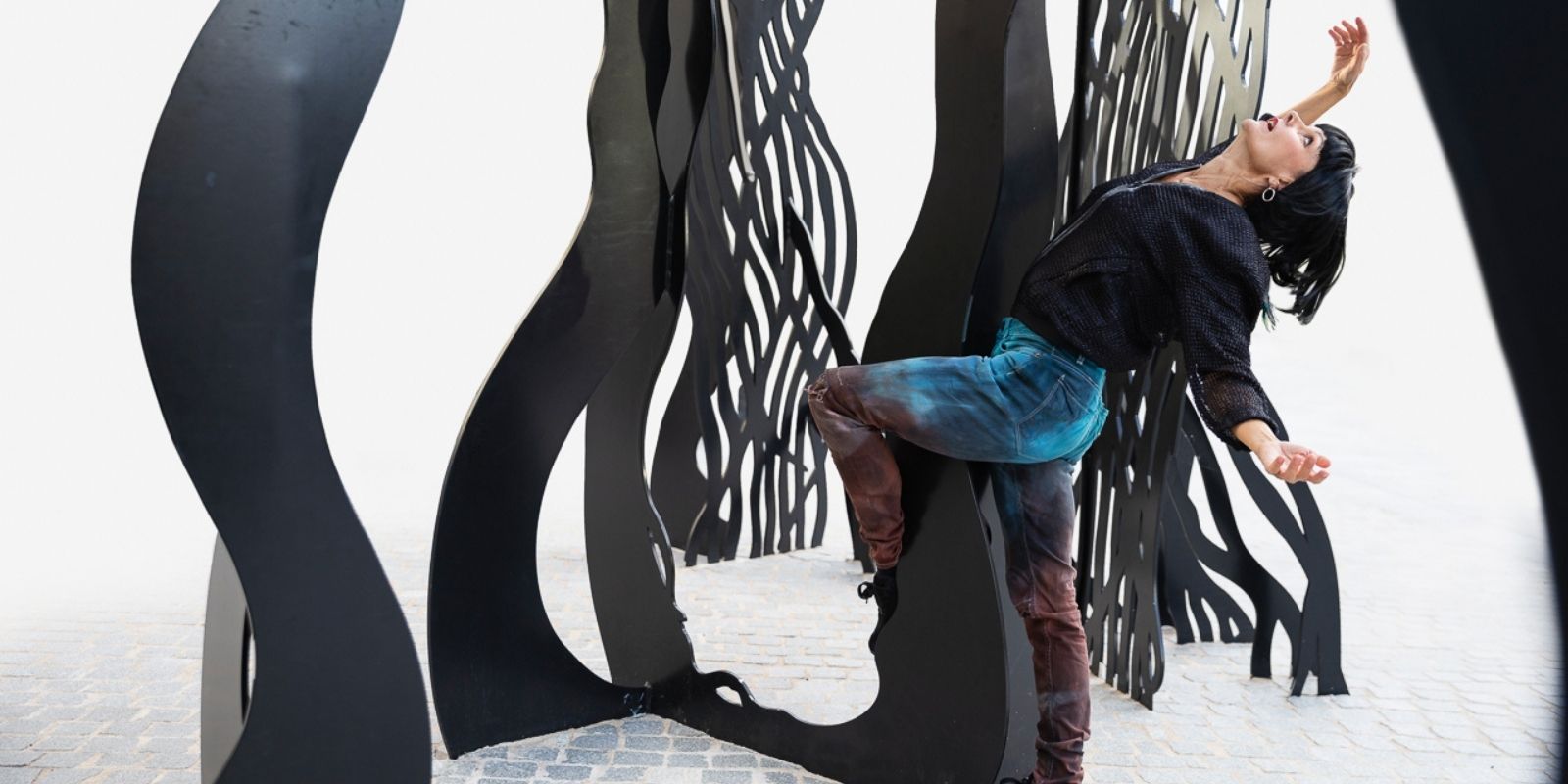 Tanssija taivuttaa vartaloaan taakse ja tanssii ison veistoksen edustalla.