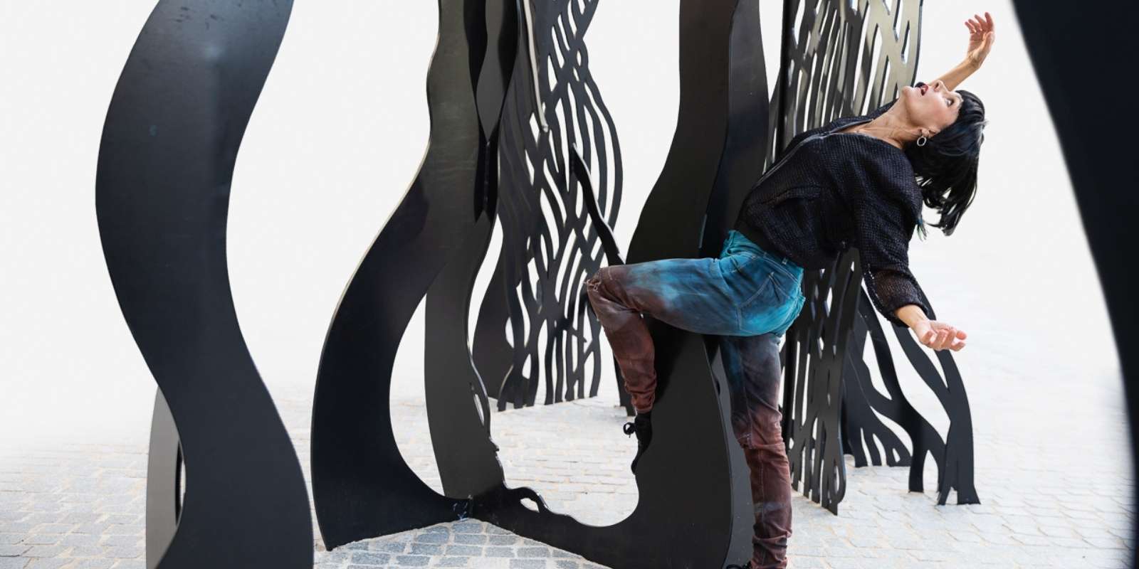 Tanssija taivuttaa vartaloaan taakse ja tanssii ison veistoksen edustalla.