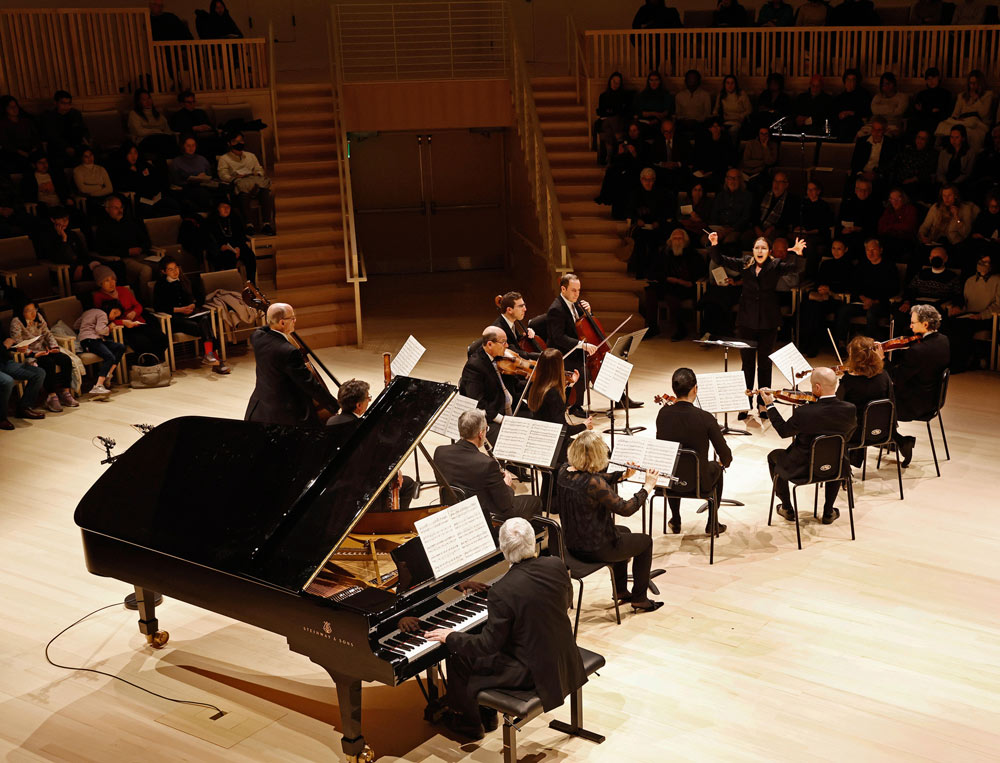 A pianist performs on stage alongside a group of string and wind musicians. Photo by Winslow Townson.