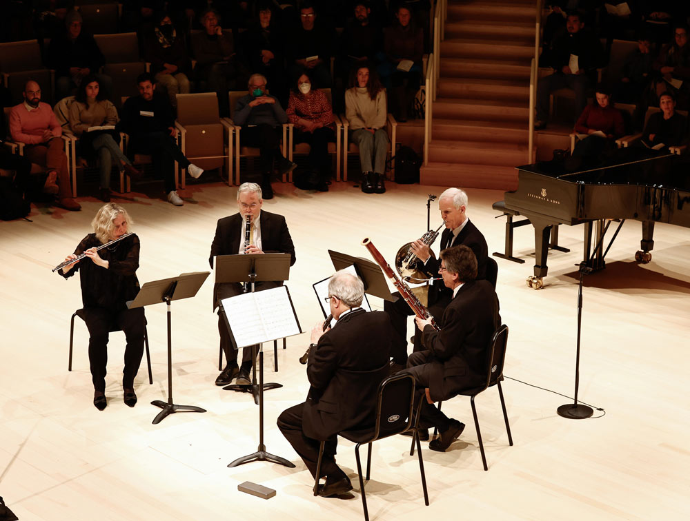 A group of wind musicians perform on stage, facing towards each other.Photo by Winslow Townson.