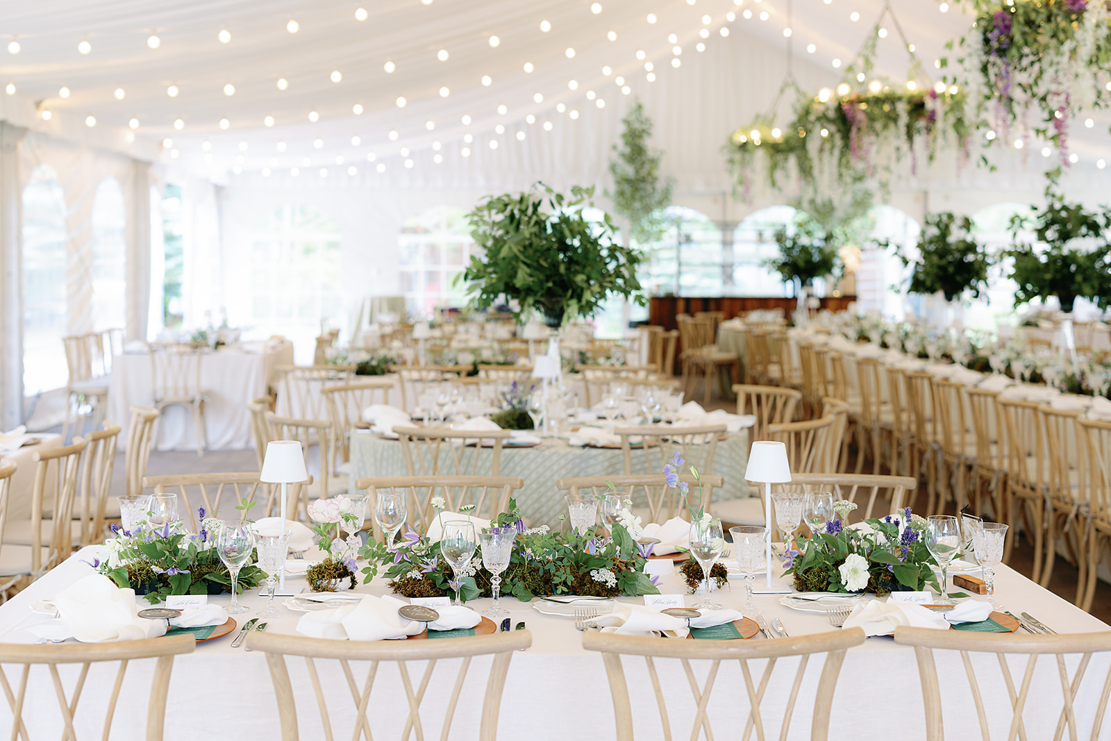 Long reception table styled with lush garden florals, wood chairs, and soft lighting at a Sun Valley tented wedding.