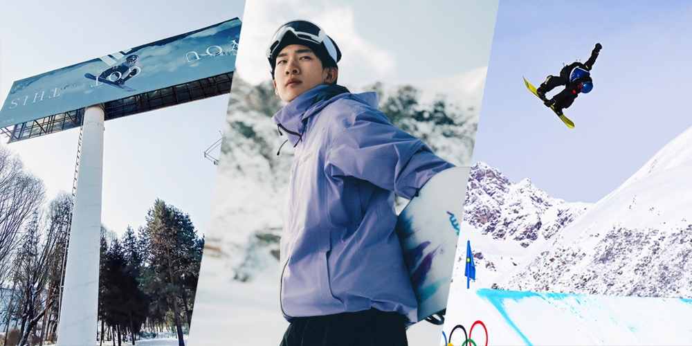 snowboarder standing in front of Olympics billboard