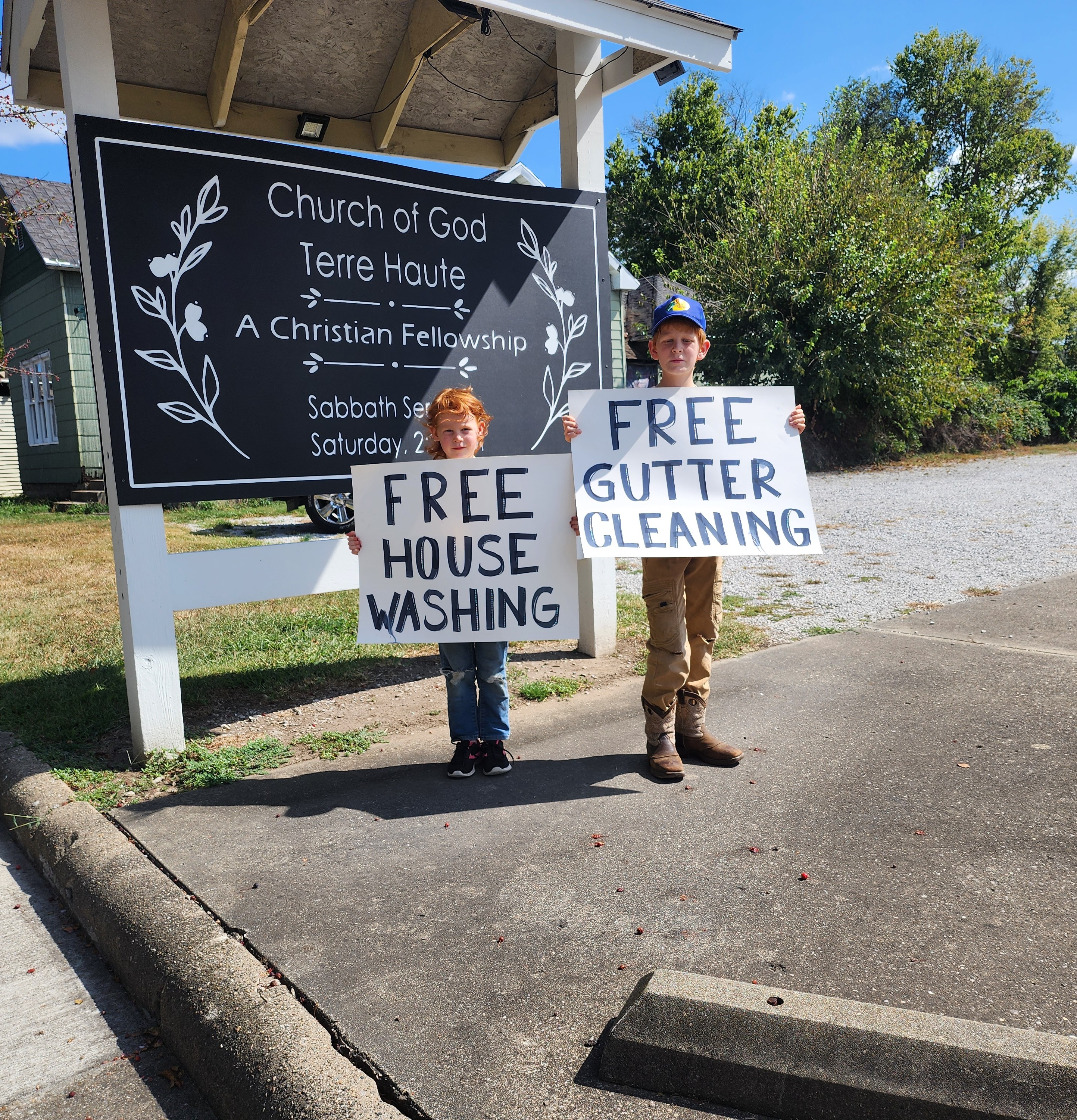 Two of our youth holding signs advertising our community outreach project (free gutter cleaning + pressure washing), September 2025.