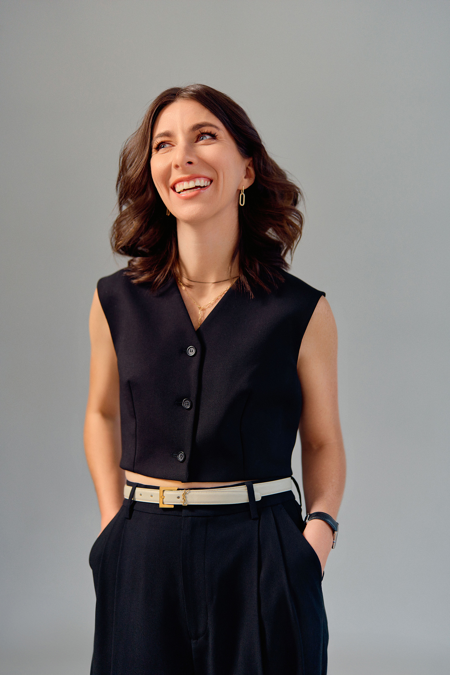 Studio portrait of Stacey McLachlan wearing a sleeveless black top and trousers, smiling and looking off to the side against a light grey background.