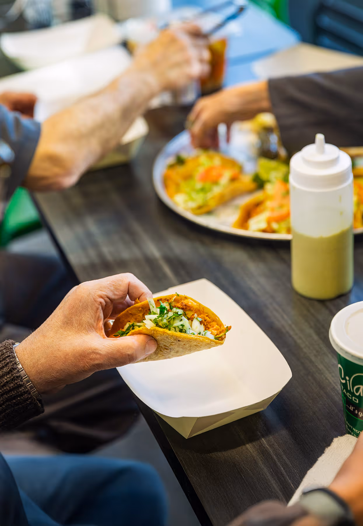 A customer enjoying an authentic Mexican taco in a casual restaurant setting. The image focuses on a taco filled with meat and cilantro, ready to be eaten, showcasing the freshness of the ingredients.