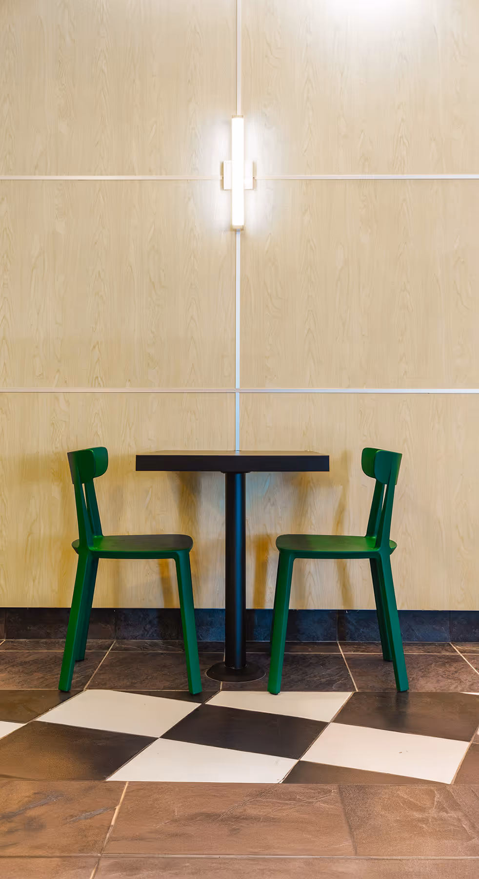 The interior design and ambiance of the restaurant, showing a minimalist table with two modern green chairs. The clean, well-lit scene highlights the contemporary style of the dining area.