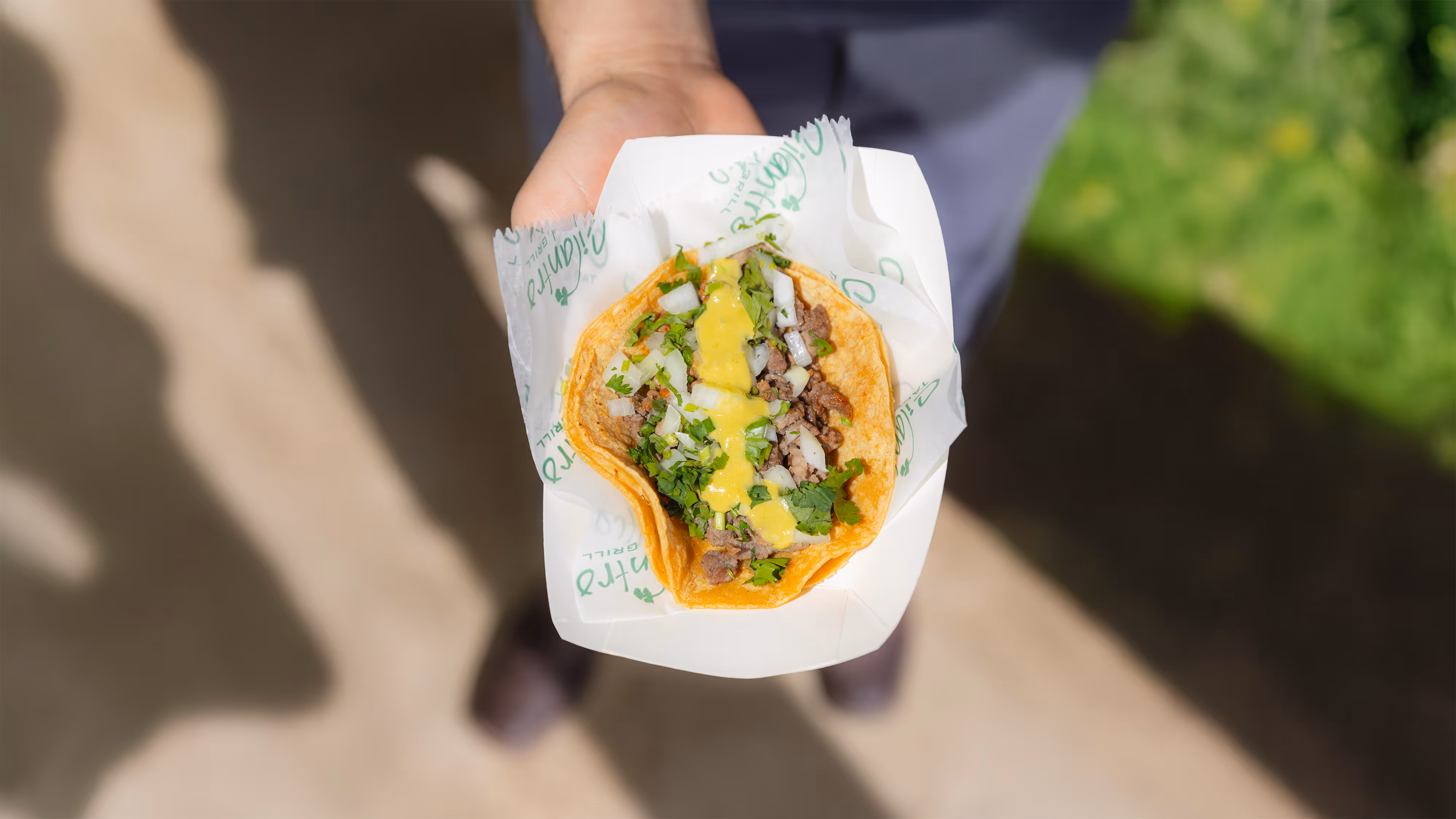 Hand holding a taco with beef, cilantro, onions, and green salsa on a corn tortilla.