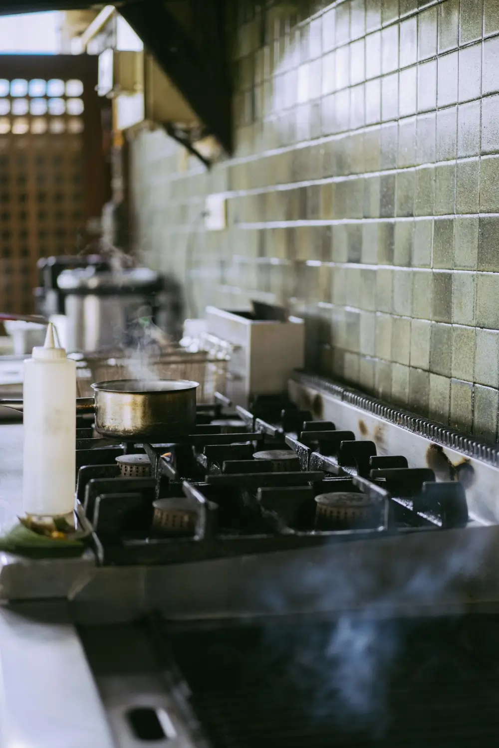 Industrial kitchen stove with a steaming pot and tiled wall background.
