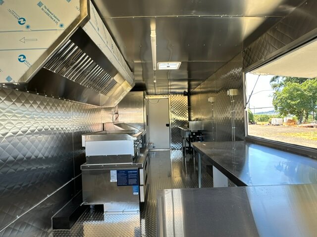 Interior of a clean, empty commercial stainless steel kitchen with cooking equipment and a large window showing an outdoor view.