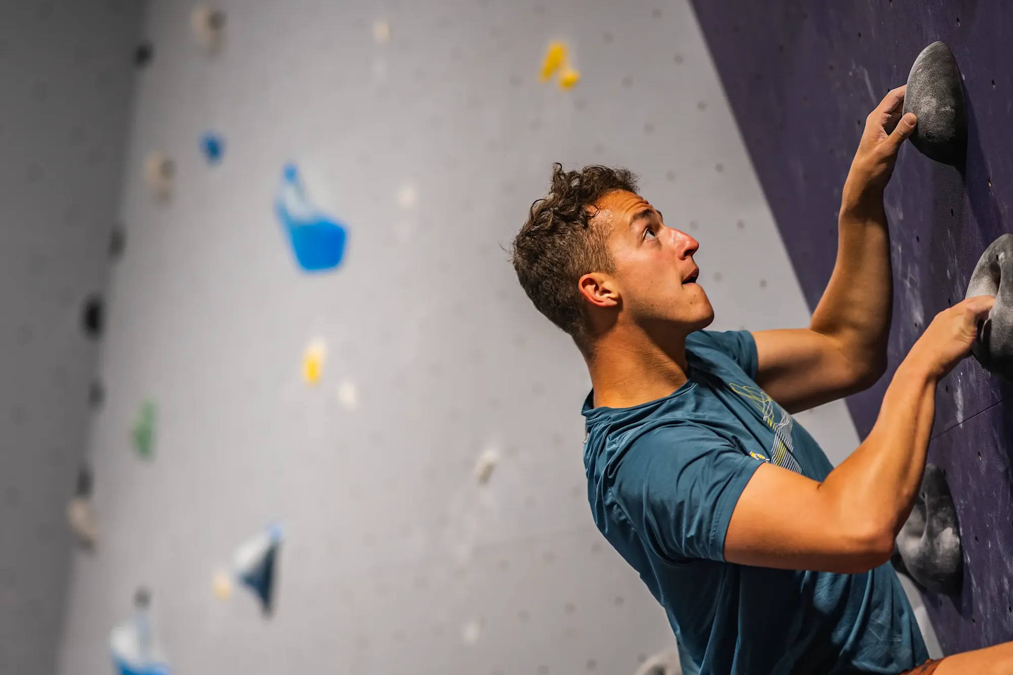 Young man focused climbing a purple indoor rock climbing wall.