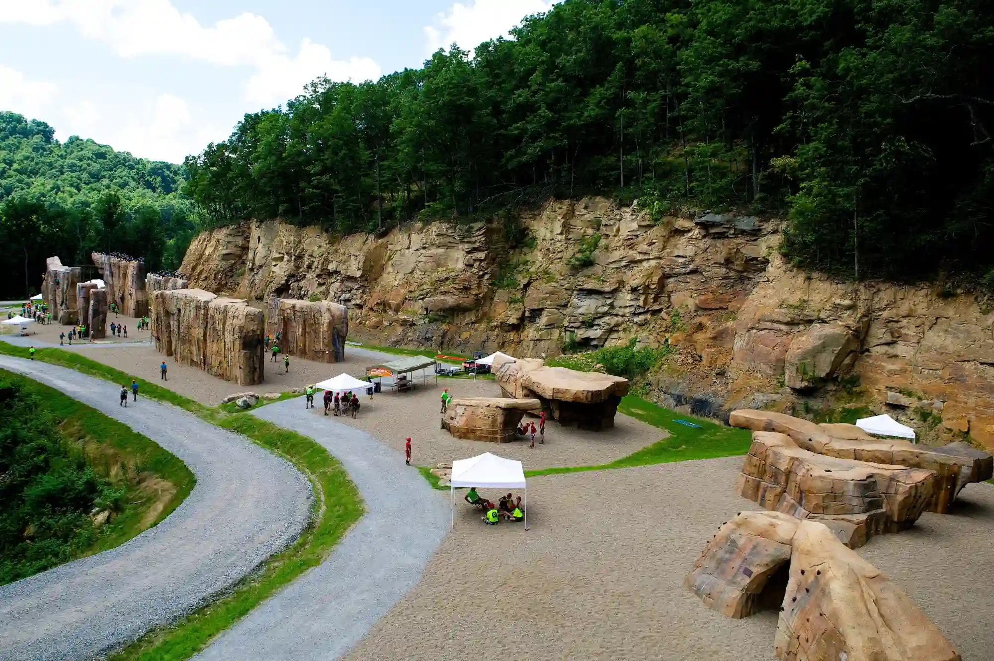 Children climbing on a large outdoor climbing boulder surrounded by green hills and a ski lift in the background.
