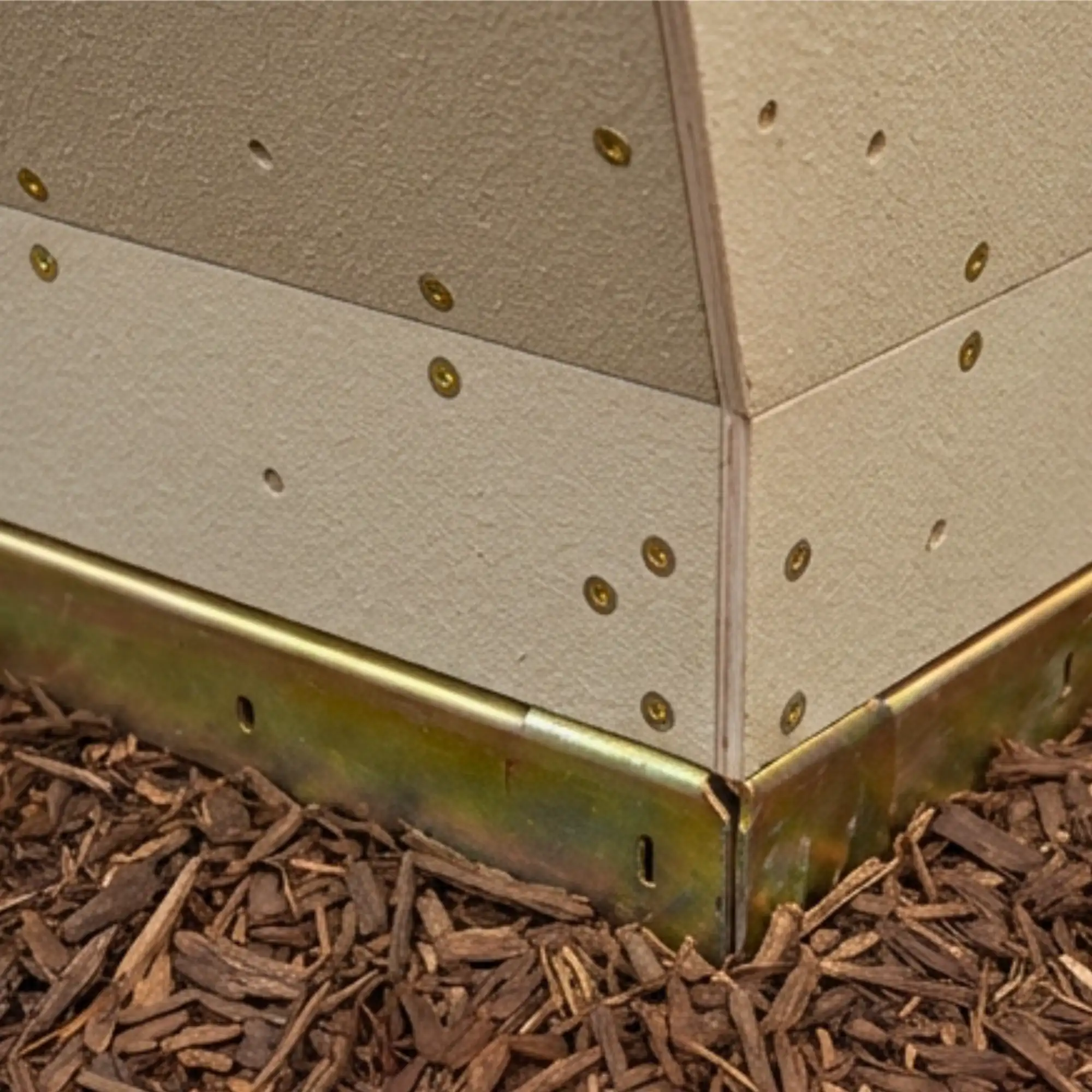 Close-up of corner joint on a pre-engineered panel secured with metal fasteners above brown wood mulch.