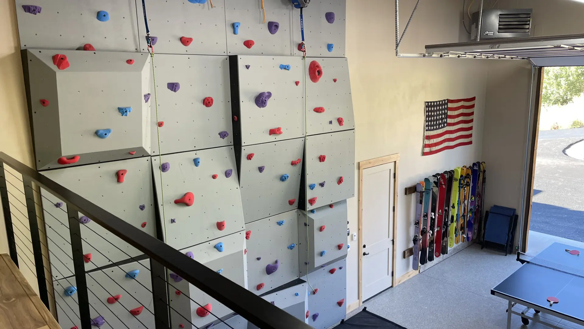 Two men assembling a large blue and yellow wooden structure outdoors on grass near a school building.
