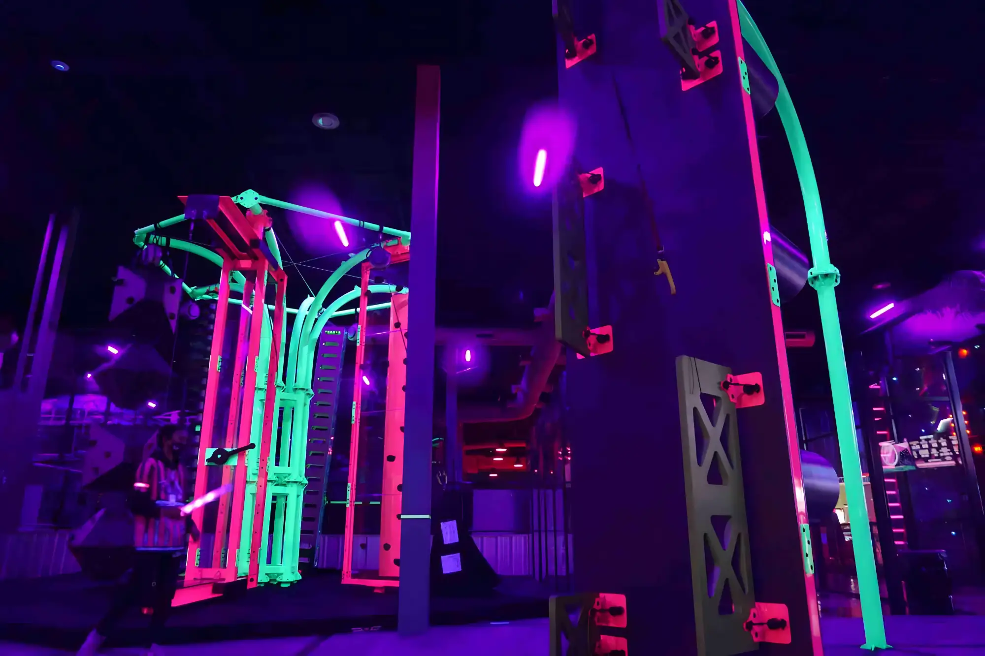Indoor climbing gym with neon-lit climbing walls and colorful structures under purple lighting.