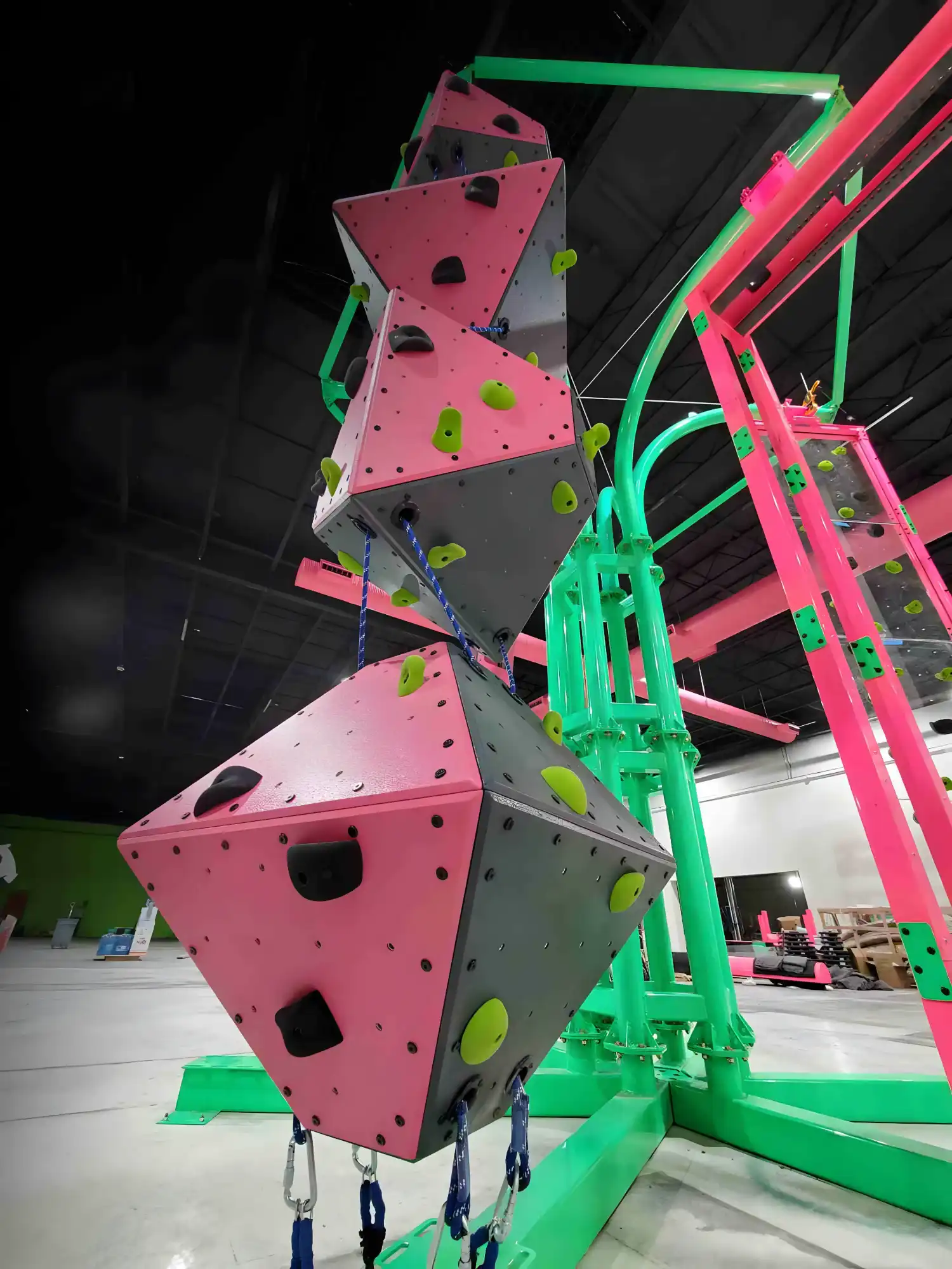 Indoor climbing structure with pink and gray geometric walls and neon green holds and framework.