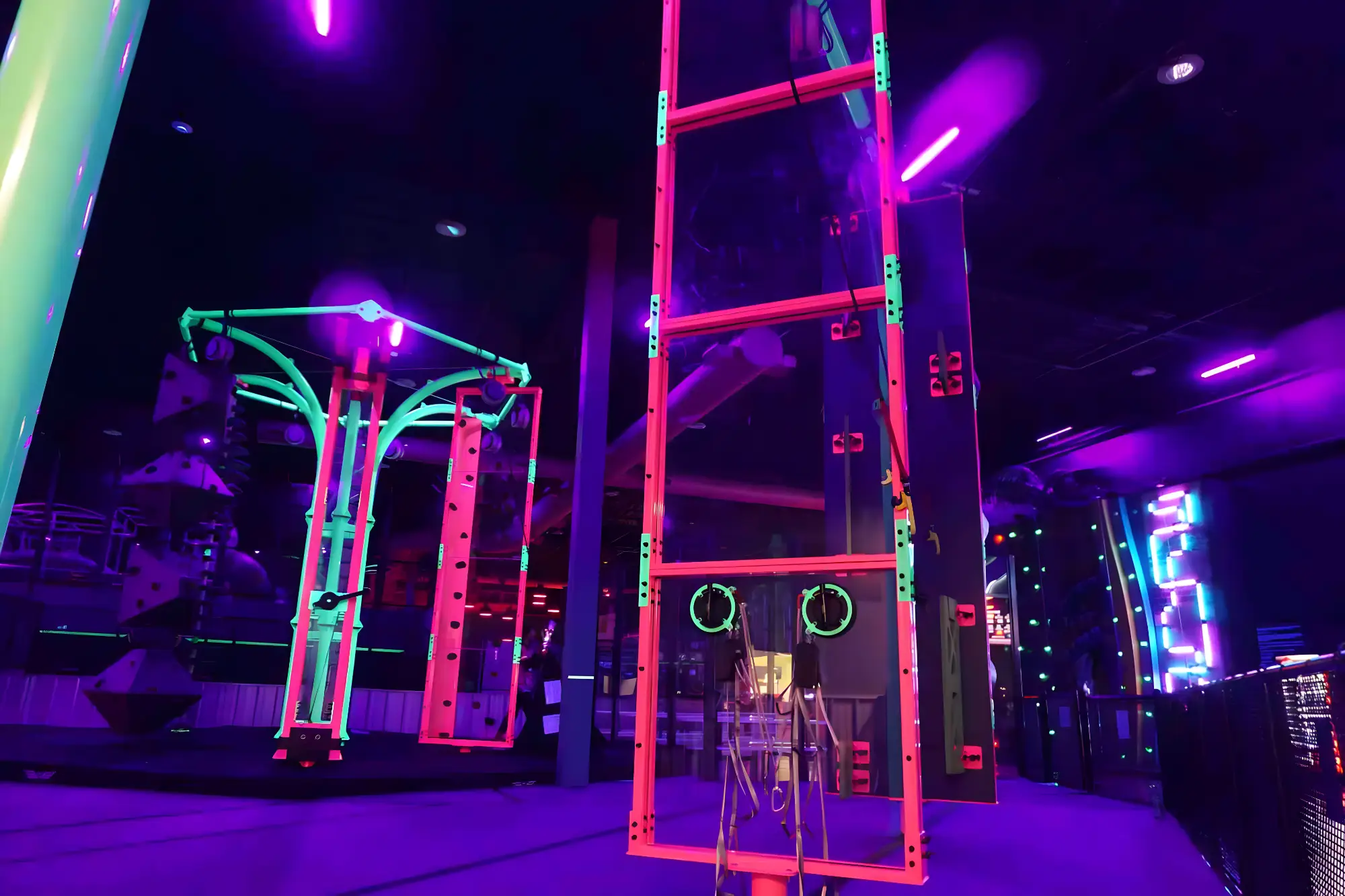 Indoor climbing gym with neon lights, climbing walls, and hanging rings in a dark setting.
