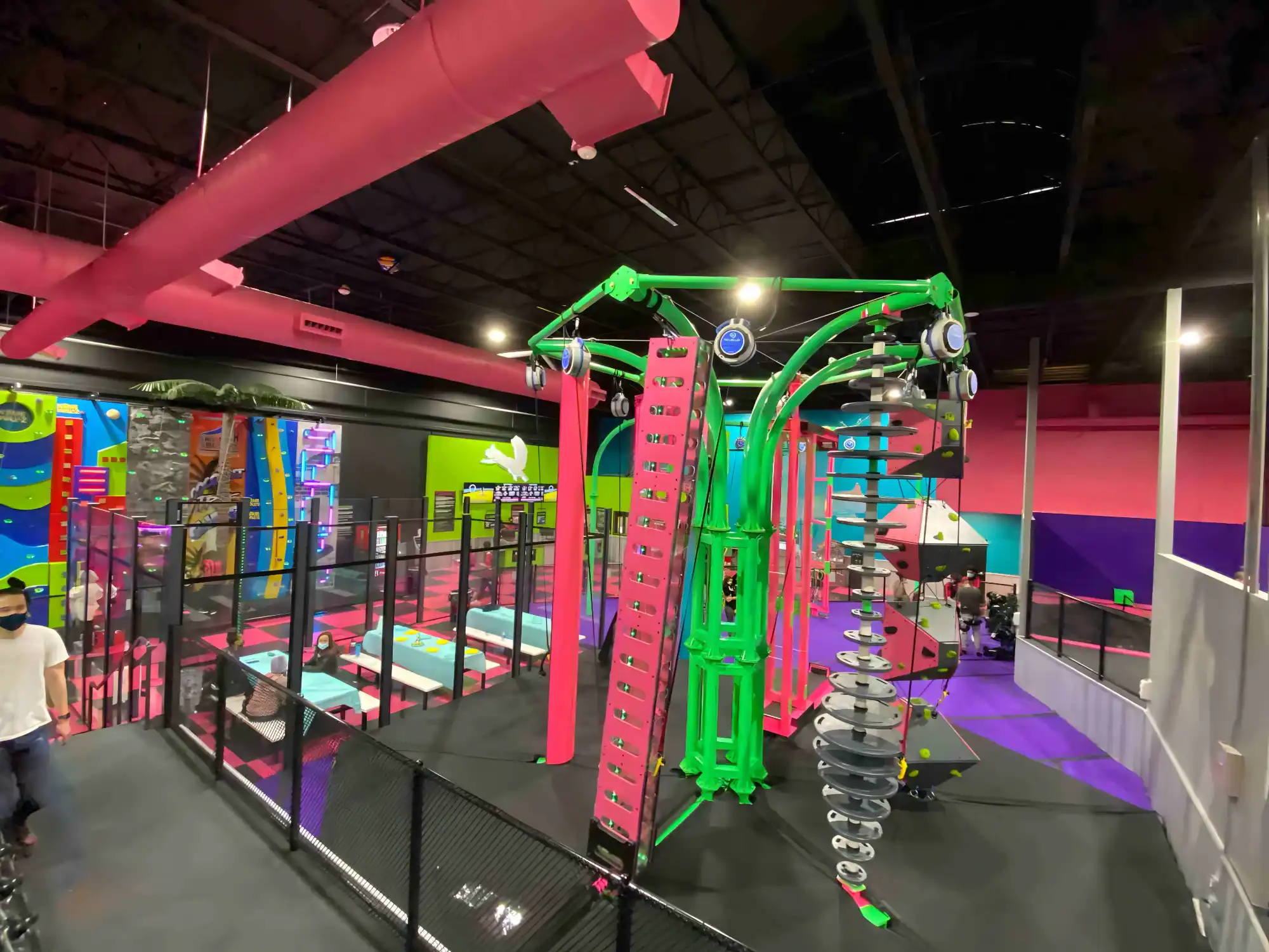 Indoor climbing gym with colorful walls, climbing structures, and people wearing masks.