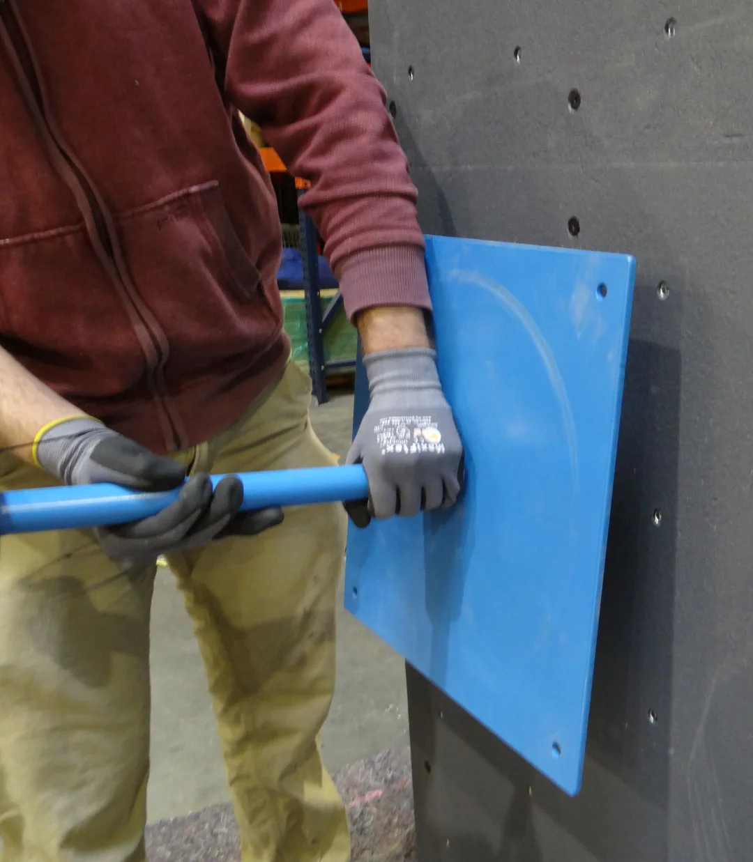 Person wearing gloves using a blue crowbar to pry a blue panel off a dark wall.
