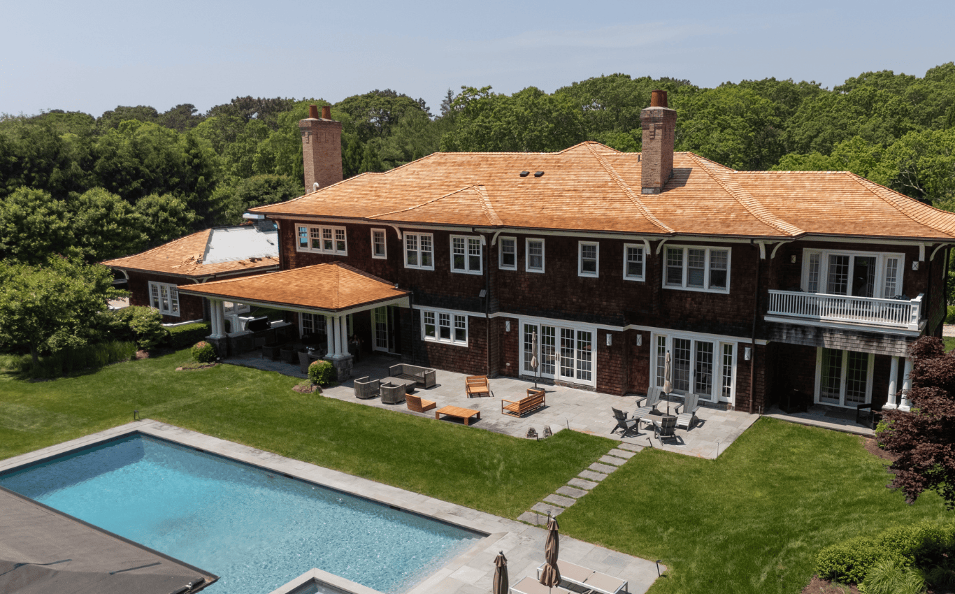Cedar-shingled luxury home with covered patio and pool area, showcasing roofing design for outdoor entertaining and seamless indoor-outdoor living