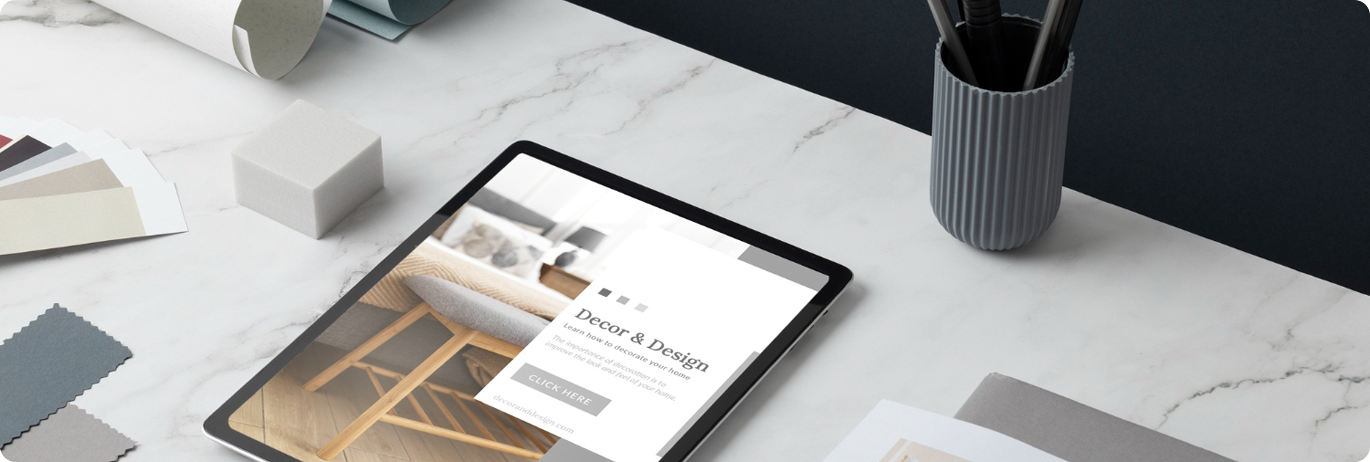 Tablet displaying home decor website on white marble desk with color swatches and a pen holder.