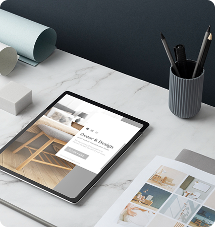 Tablet on marble table displaying interior design site, surrounded by magazines and pencils.