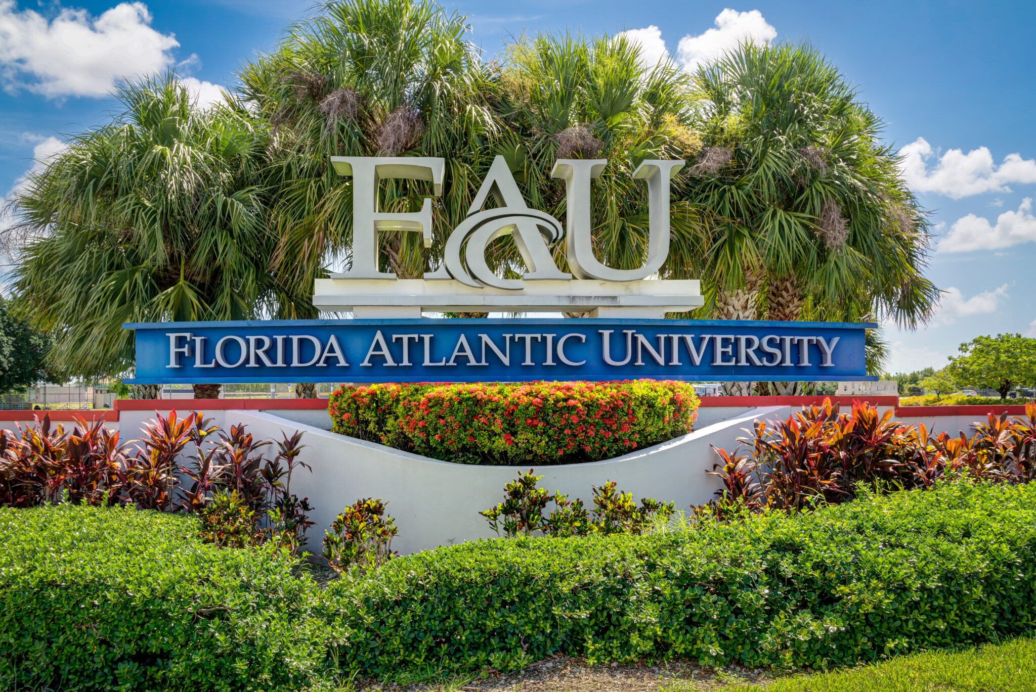 Florida Atlantic University sign with large FAU letters, set against palm trees and surrounded by colorful landscaping at the Boca Raton campus entrance..