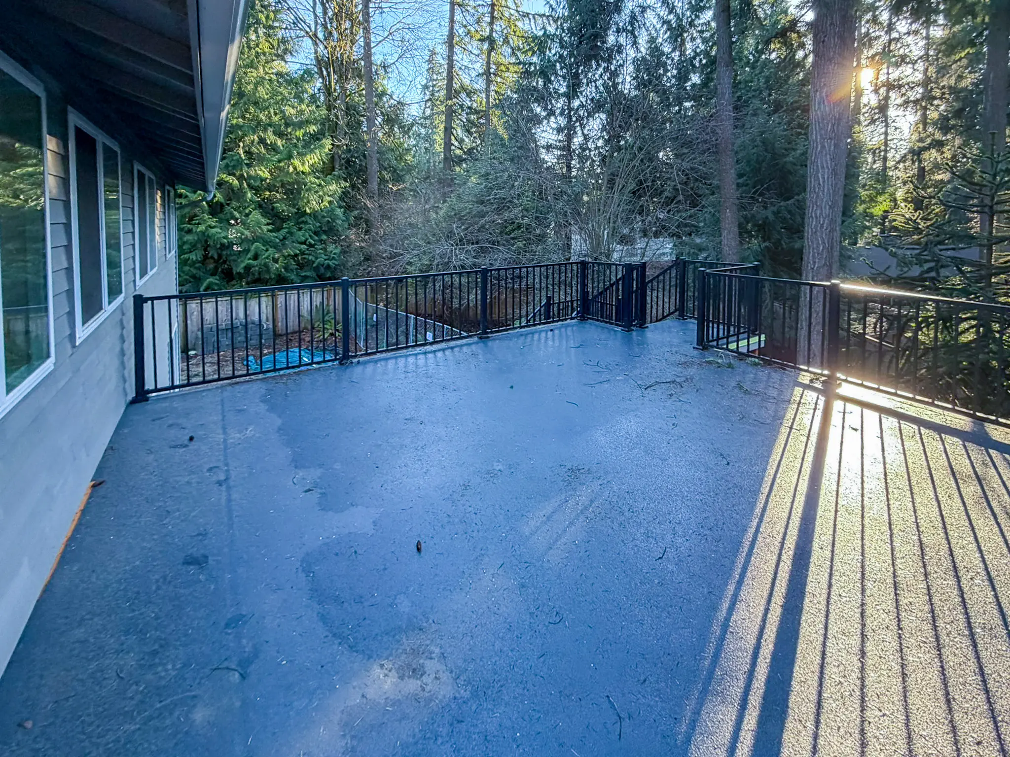 Existing elevated deck with black metal railing surrounded by trees on a Kirkland, WA home before construction.