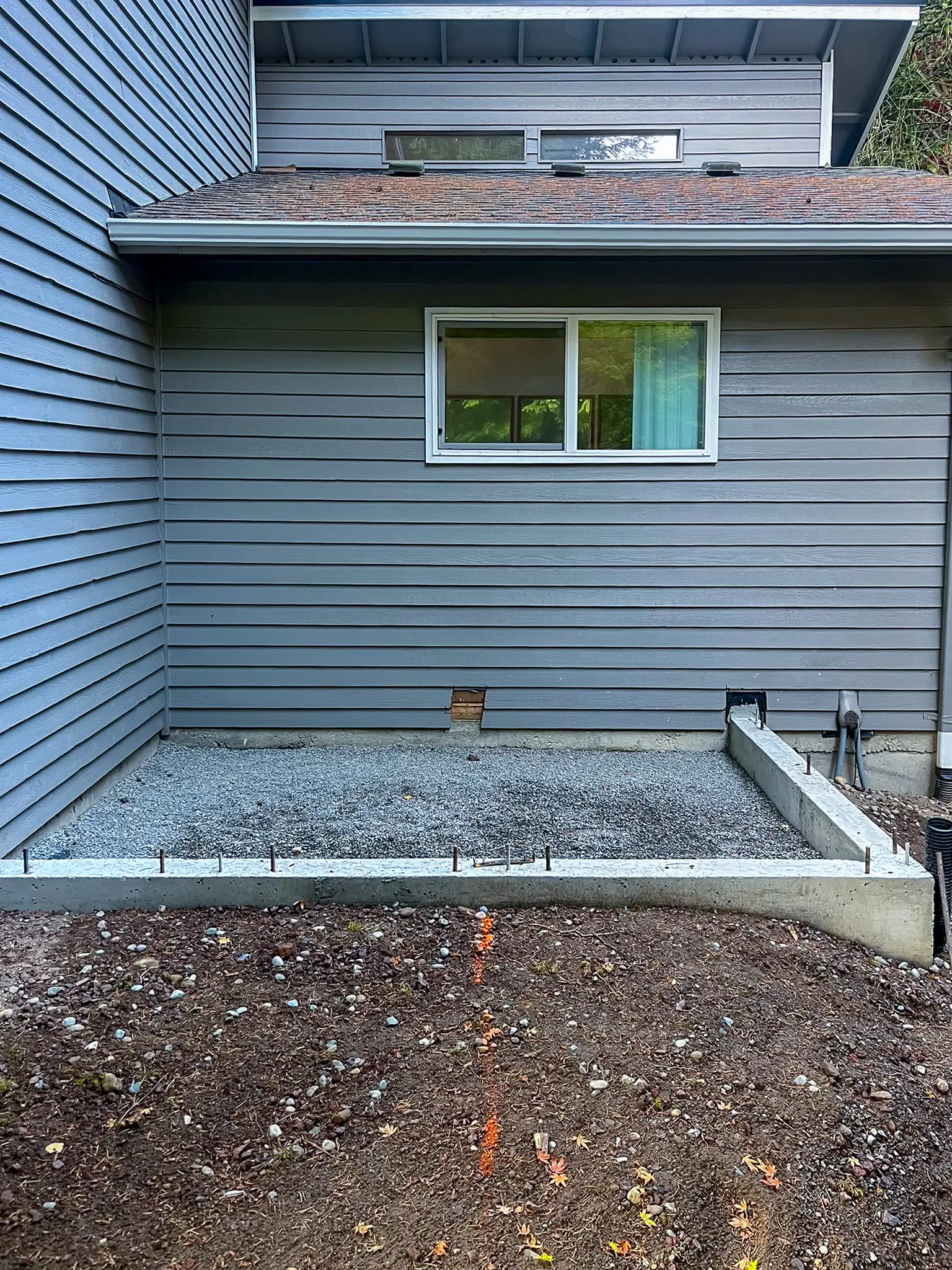 New concrete foundation footing and gravel base against the exterior wall of a Kirkland, WA home during early construction.