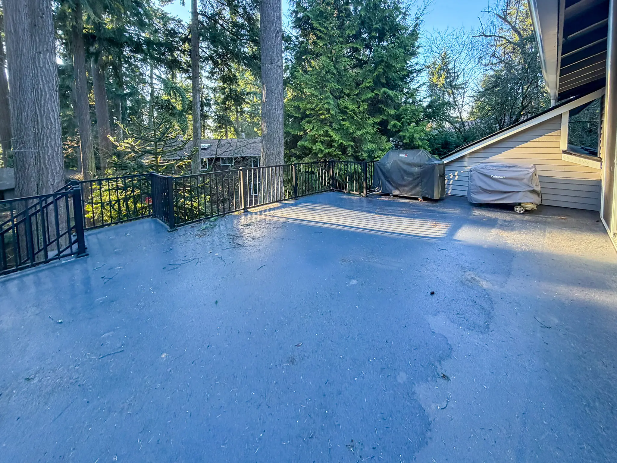 Existing elevated deck with black metal railing and two covered grills on a Kirkland, WA home before construction.