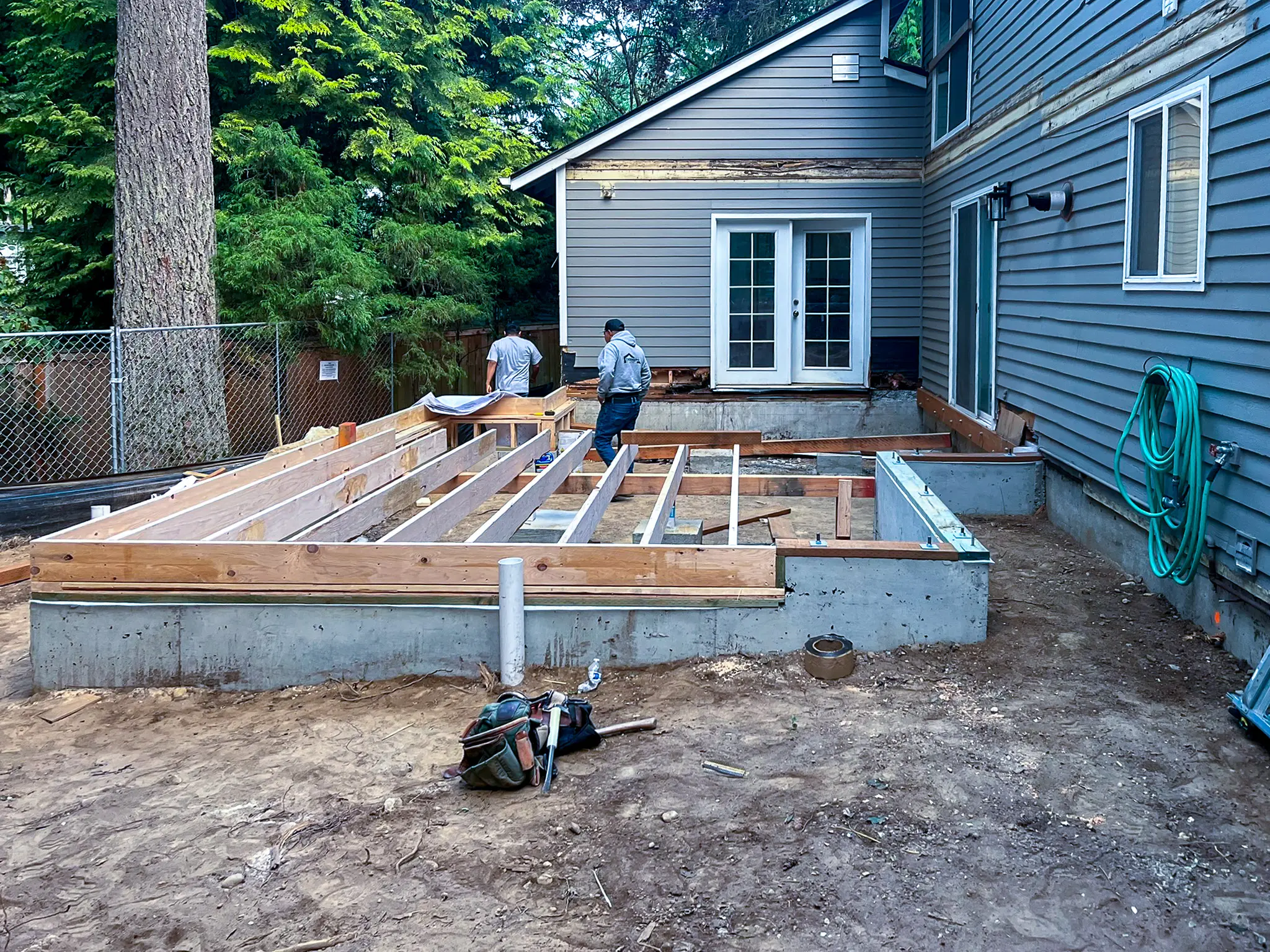 New concrete foundation and wood floor framing under construction, with two workers on site.